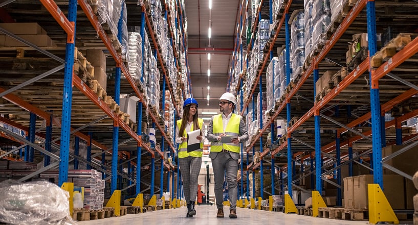 workers-with-hardhats-reflective-jackets-walking-through-big-warehouse-aisle-checking-goods-condition